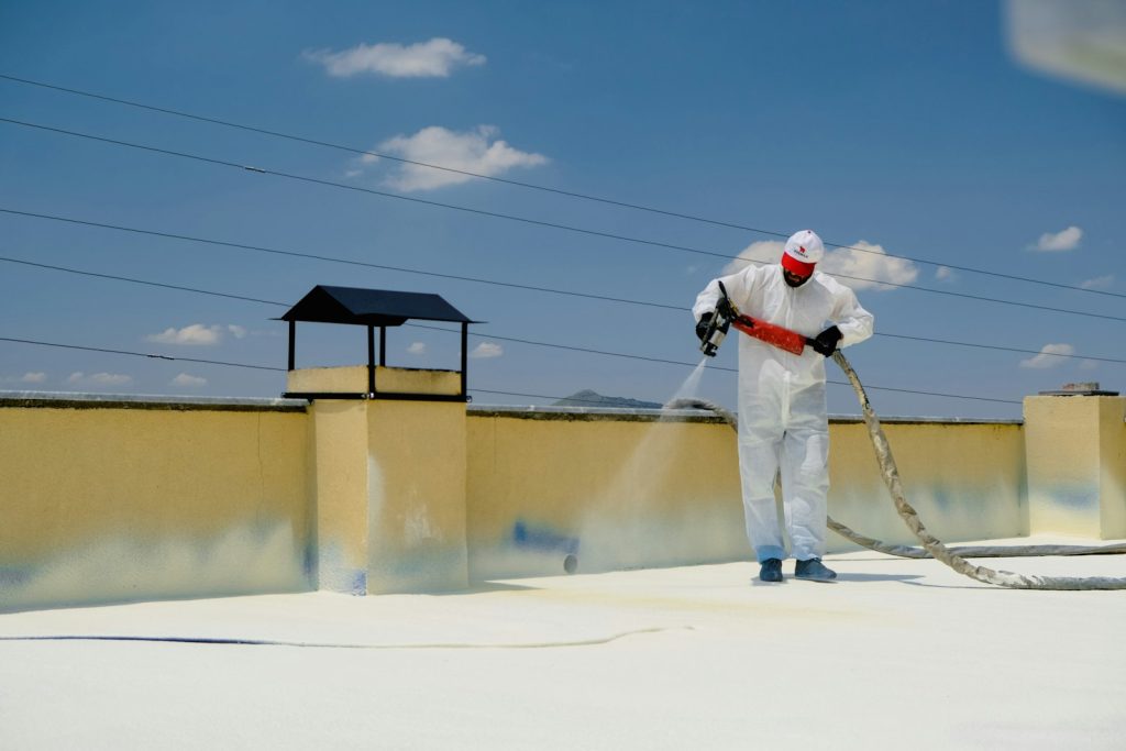 Installer in protective coveralls spraying foam under a roof deck